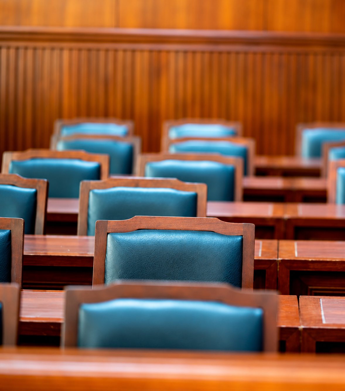 Des rangées de chaises en bois à assise et dossier en cuir vert devant des bureaux en bois, dans une salle aux boiseries chaudes.